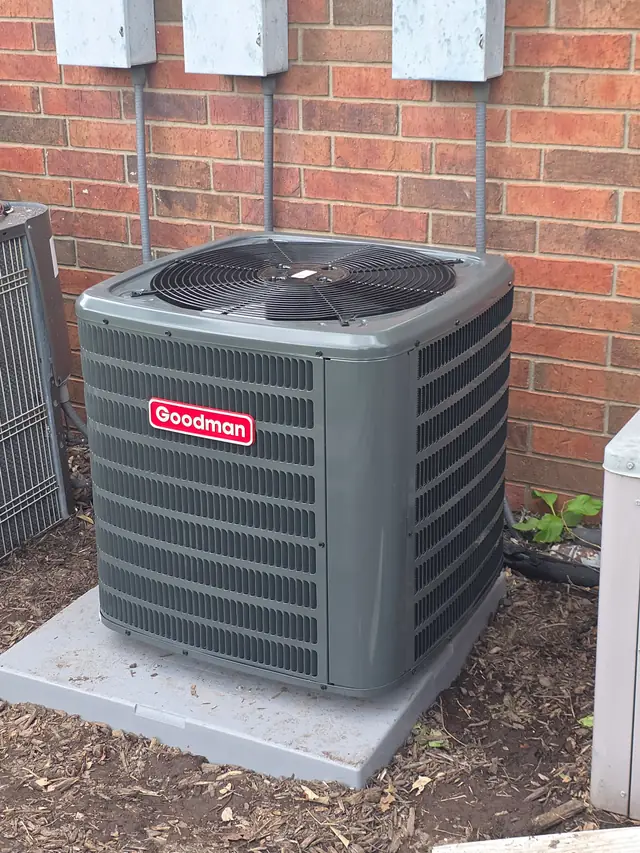 A Goodman condenser on a concrete pad against brick