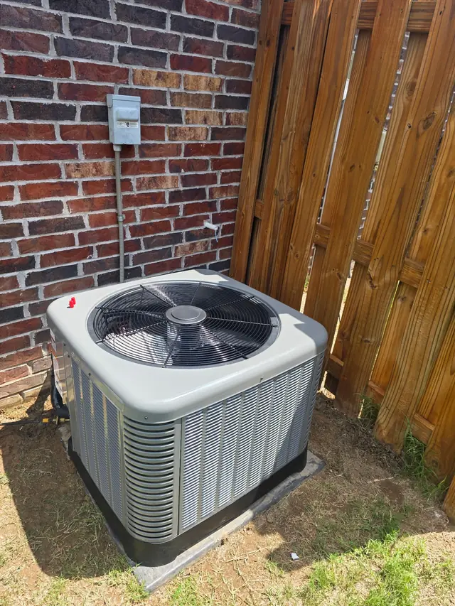A condenser on a pad between brick and a cedar privacy fence
