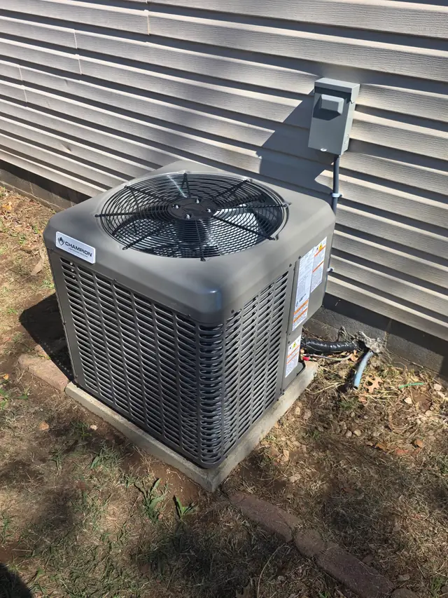 A new condenser on a pad beside grey siding
