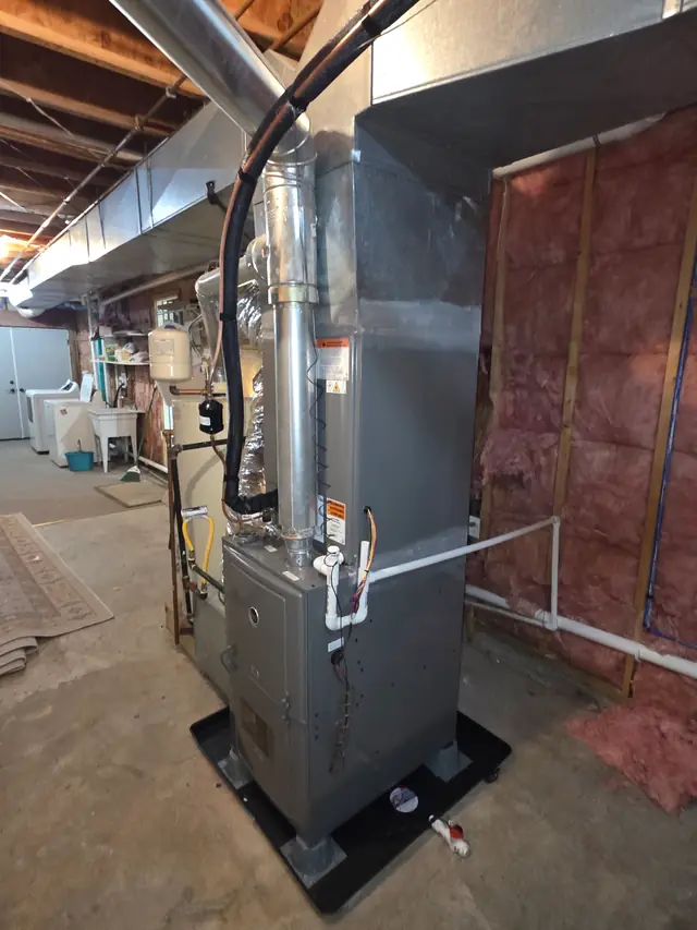A new gas furnace on a stand in an unfinished basement, with a fresh sheet-metal plenum and flue pipe